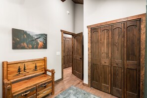 A hallway with a wooden bench, a painting of a forest, and a set of wooden doors. - Peaceful Seasons – A Cozy Mountain Retreat with Modern Comforts (Murphy)