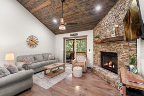 A living room with a stone fireplace, a sofa, a chair, and a coffee table. - Peaceful Seasons – A Cozy Mountain Retreat with Modern Comforts (Murphy)