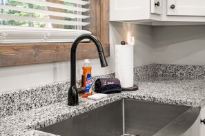 A kitchen with a black sink, a window with blinds, a bottle of Ajax dish soap, and a towel. - Peaceful Seasons – A Cozy Mountain Retreat with Modern Comforts (Murphy)