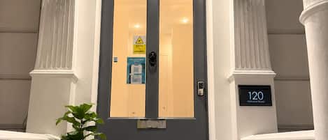 A hotel entrance with a grey door, number 120, a CCTV warning sign, and a potted plant on the left.