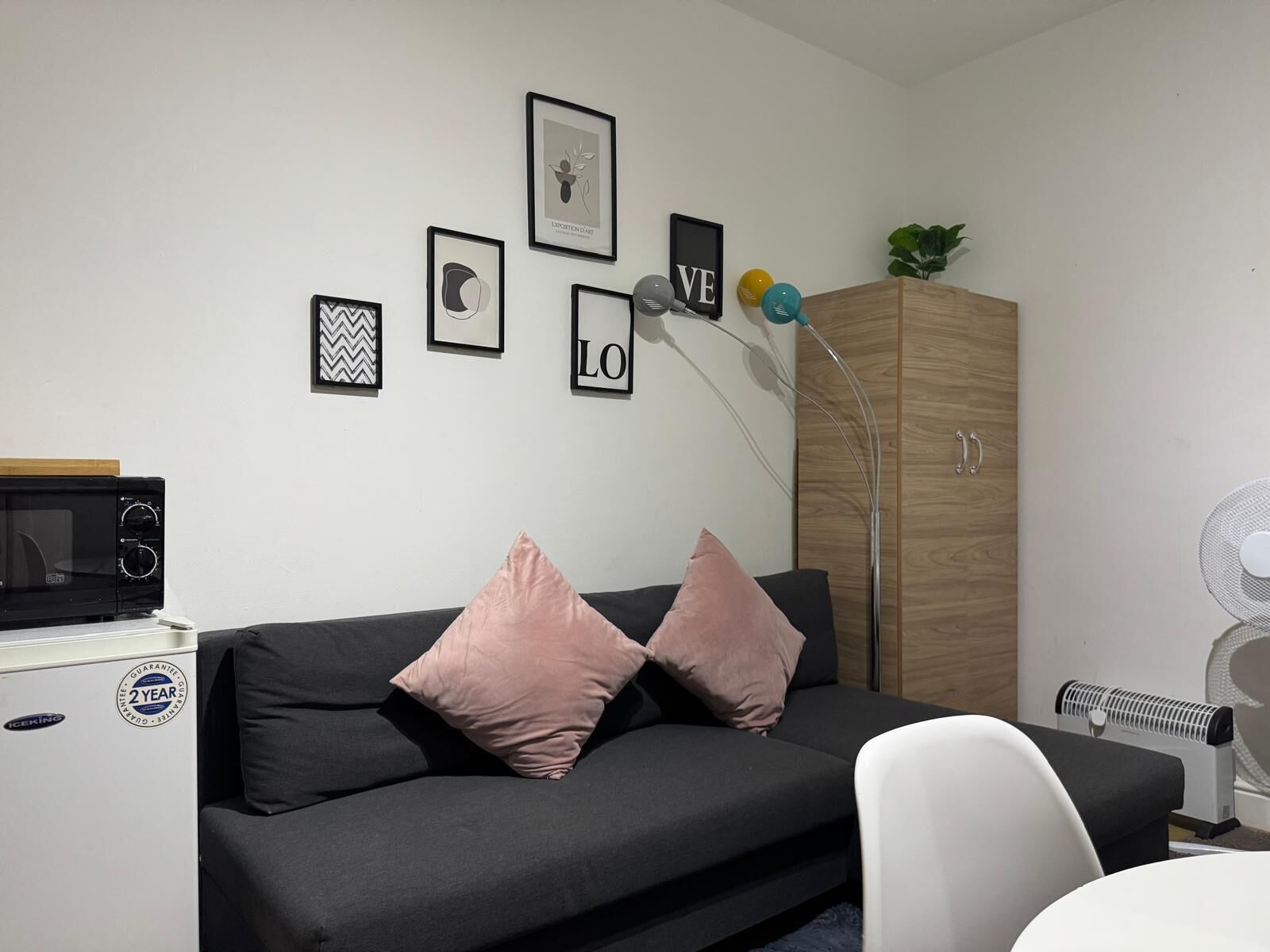 A modern living room with a black sofa, two pink cushions, a wooden cabinet, and a white chair.