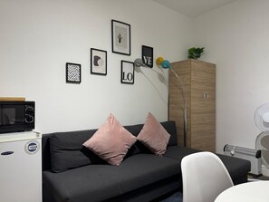 Uma sala de estar moderna com um sofá preto, duas almofadas cor-de-rosa, um aparador de madeira e uma cadeira branca.