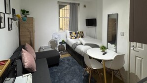 A compact living space with a bed, a sofa, a small table, and a TV. - Cozy Flats Near Olympia and Westfield (London)