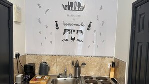 A compact kitchen with a stainless steel sink, a coffee maker, a kettle, and a stove. - Cozy Flats Near Olympia and Westfield (London)