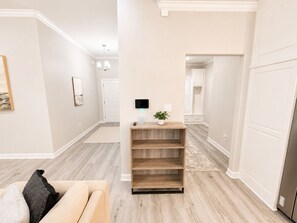 A hallway with a wooden bench, a flat-screen TV mounted on the wall, and a potted plant on the bench.