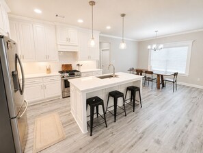 A modern kitchen with white cabinets, a stainless steel refrigerator, a gas stove, and a large island with bar stools.