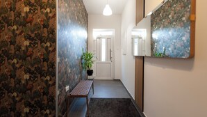 A hallway with patterned wallpaper, a bench, a potted plant, and a door with a light fixture above it. - A comfortable family room with secure parking near the city center. (Subotica)