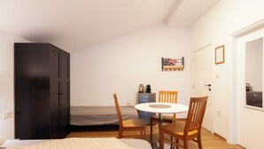 A compact bedroom with a bed, a small table with chairs, a wardrobe, and a kitchenette. - A comfortable family room with secure parking near the city center. (Subotica)