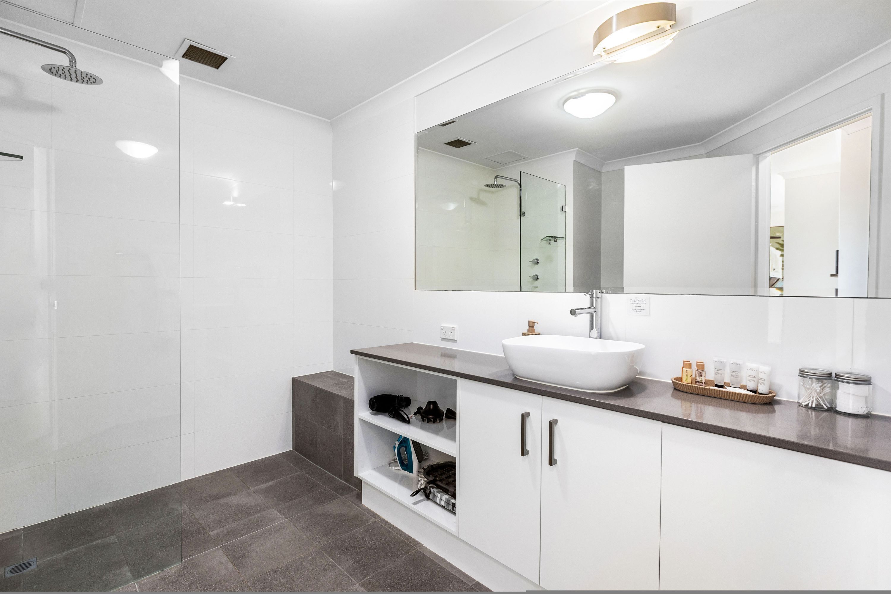 A modern bathroom with a walk-in shower, a large mirror, and a vanity with a sink.