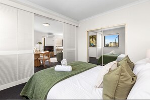 A hotel room with a bed, a desk, and a chair. There is a window with a view of buildings. - Rest and Roam - A Executive Sepal Stay (Perth)