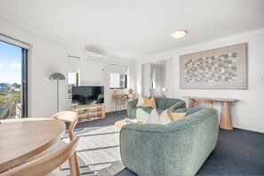 A modern living room with a flat-screen TV, green sofas, a wooden coffee table, and a large abstract painting. - Rest and Roam - A Executive Sepal Stay (Perth)