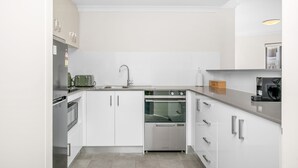 A modern kitchen with white cabinetry, stainless steel appliances, and a built-in oven. - Rest and Roam - A Executive Sepal Stay (Perth)