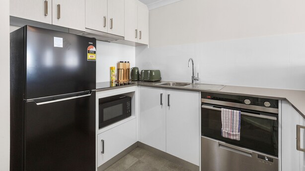 A modern kitchen with a black refrigerator, microwave, and oven, white cabinets, and a stainless steel sink. - Rest and Roam - A Executive Sepal Stay (Perth)