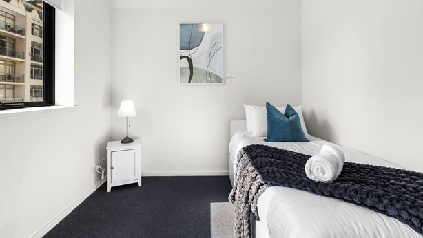 A bedroom with a bed, a bedside table with a lamp, a window, and a wall-mounted artwork. - Rest and Roam - A Executive Sepal Stay (Perth)