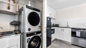 A compact kitchen with a washing machine, a refrigerator, and a stove. - Rest and Roam - A Executive Sepal Stay (Perth)