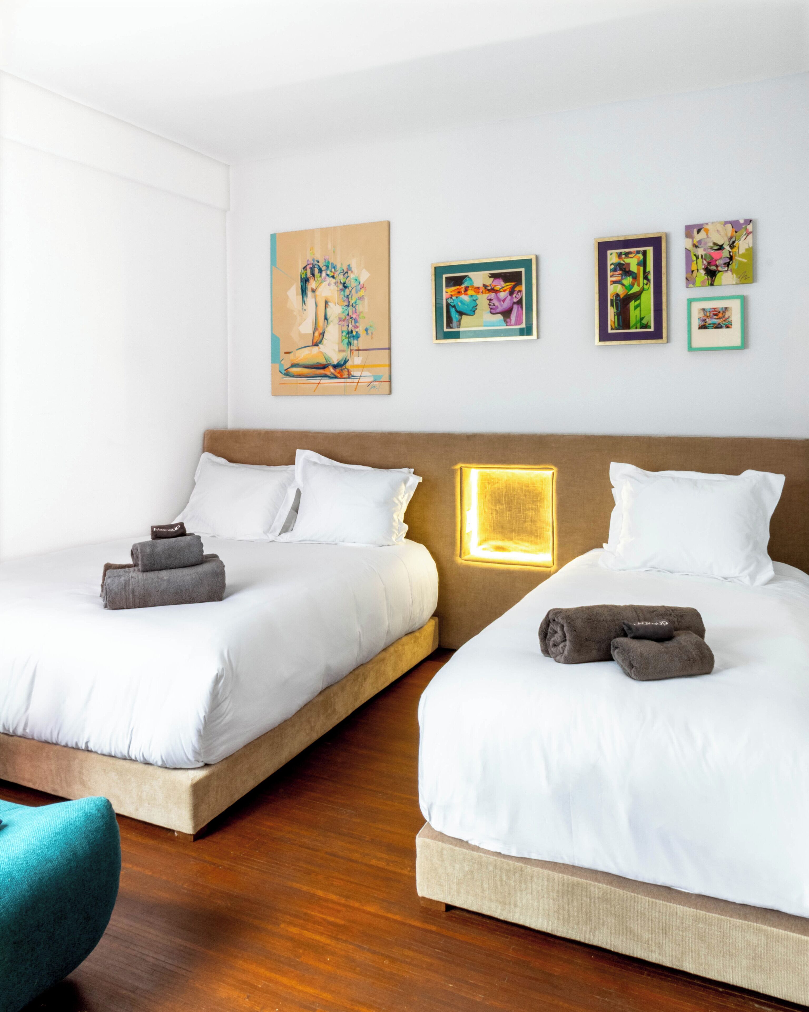 A hotel room with two beds, a wooden floor, and artwork on the wall.