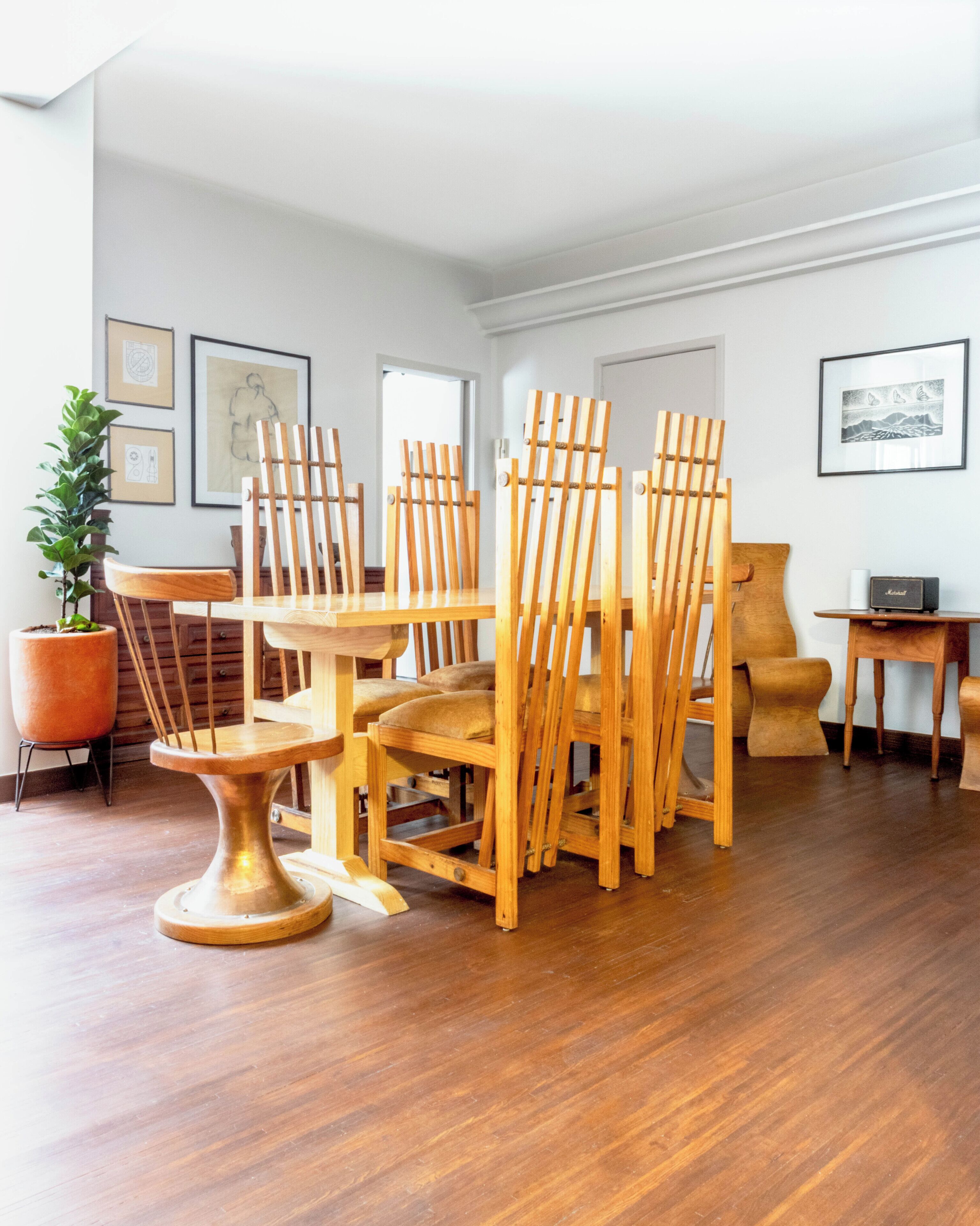 A spacious room with wooden flooring, a dining table, multiple chairs, a potted plant, and framed artwork on the walls.