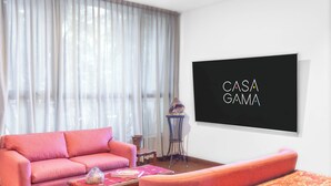 Ein Wohnzimmer mit einem rosa Sofa, einem Couchtisch, einem gemusterten Teppich und einem an der Wand befestigten Flachbildfernseher.