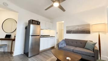 Un espacio habitable compacto con kitchenette, un sofá, una mesa de centro y un ventilador de techo.