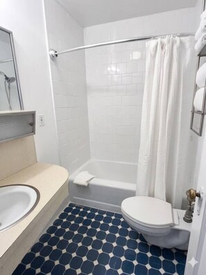 Un baño con inodoro blanco, bañera y ducha con cortina blanca.