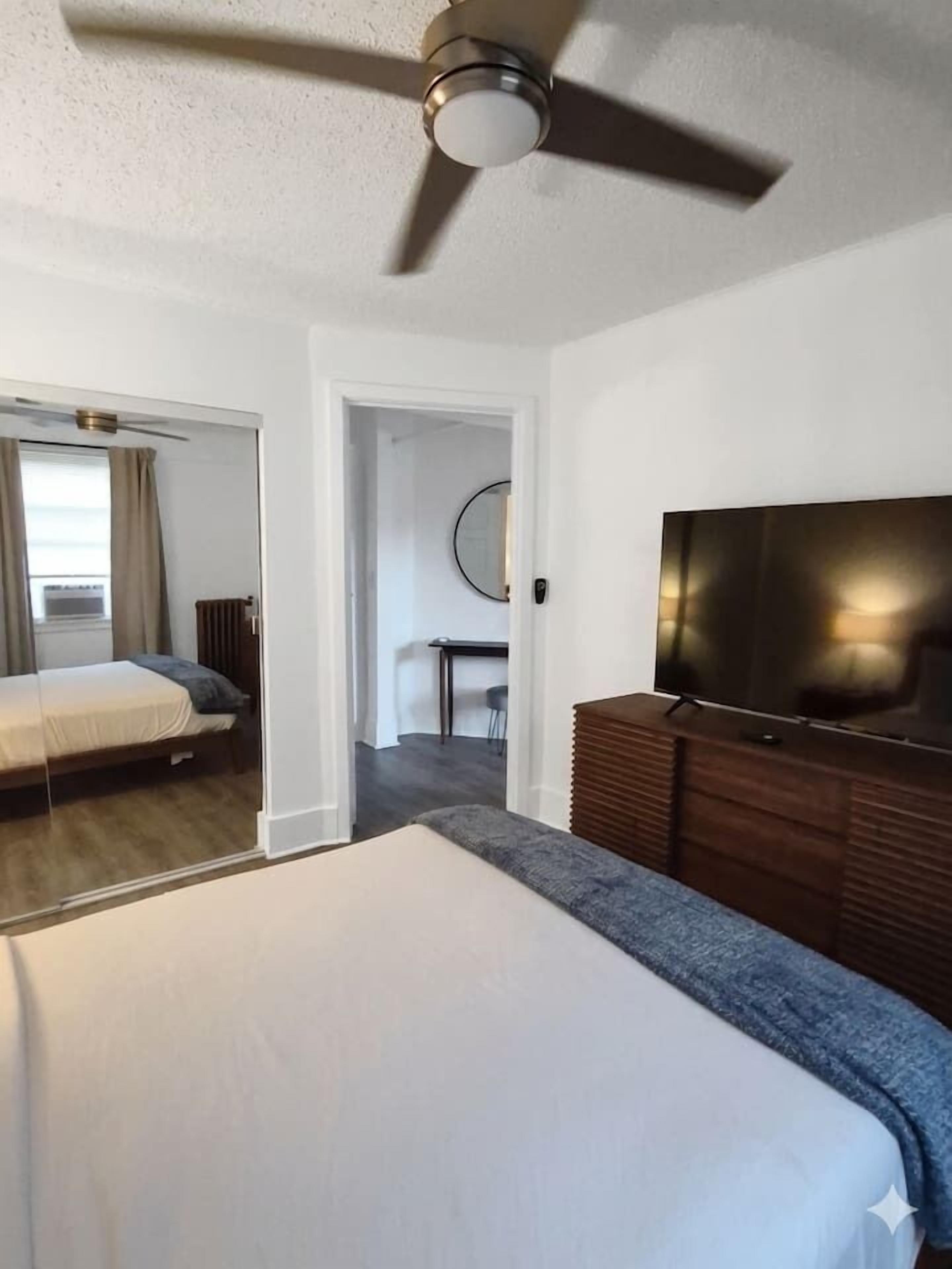 Una habitación de hotel con cama, televisor y ventilador de techo.