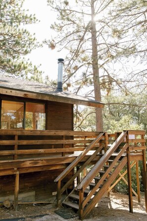 Eine Holzhütte mit Schornstein, einer Holzterrasse und einer Treppe zum Eingang.
