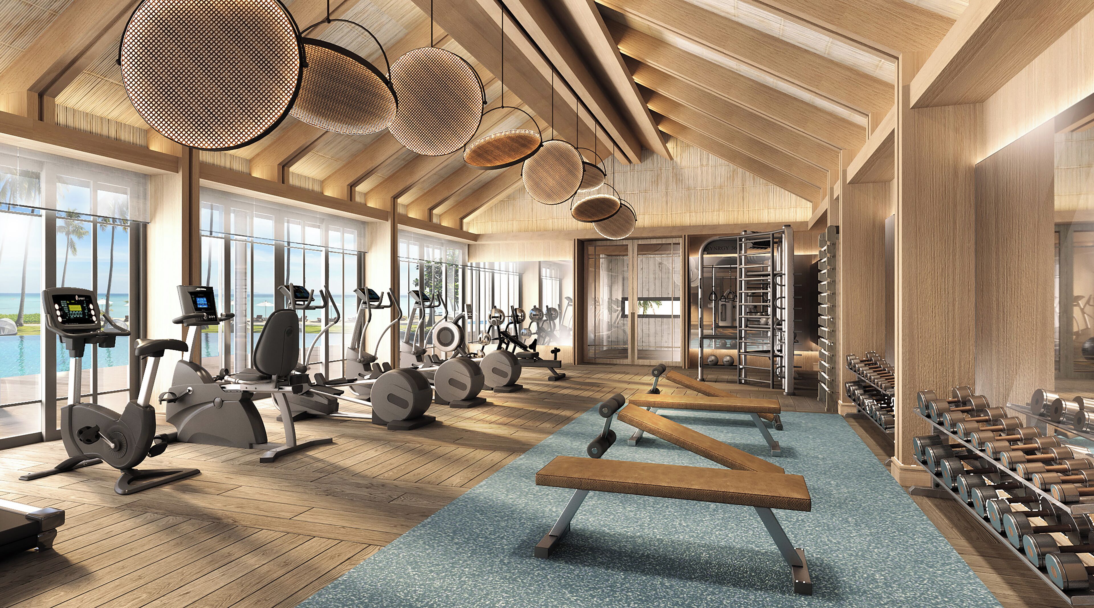 A modern gym with various exercise equipment, large windows, and a wooden interior.
