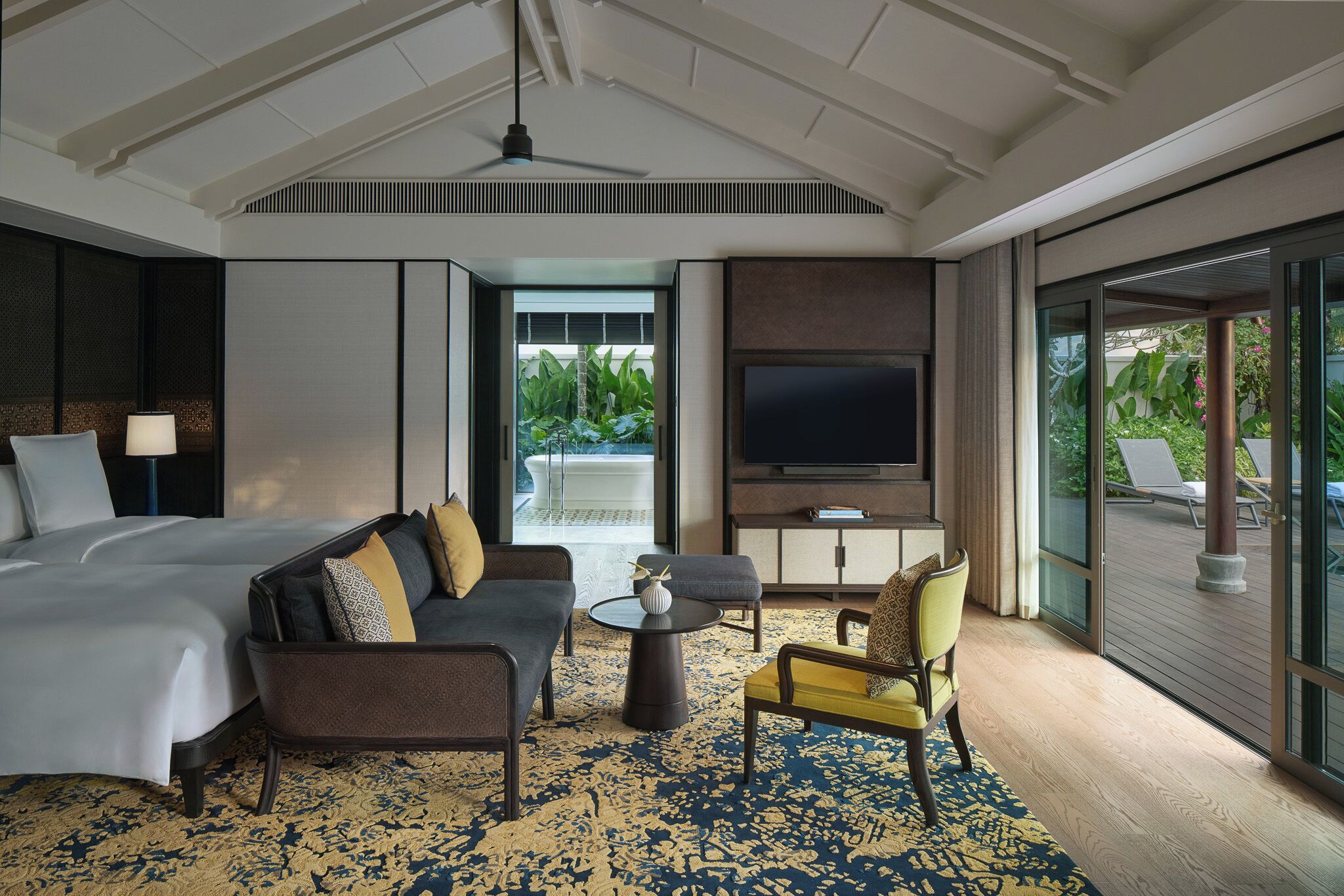 A hotel room with a bed, sofa, armchair, and a TV.