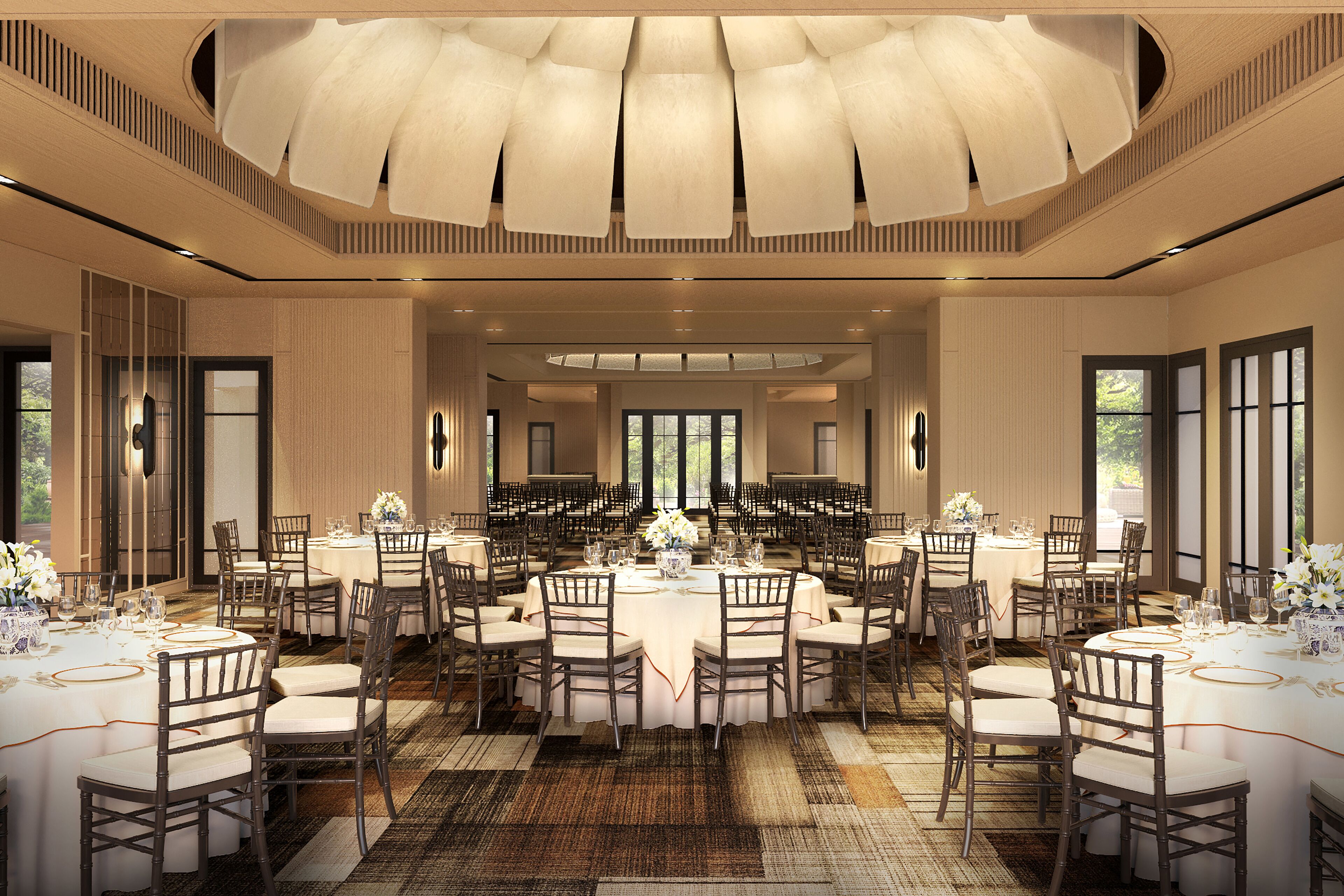 A spacious banquet hall with multiple round tables, chairs, and a high ceiling with a central light fixture.
