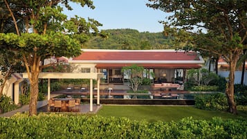 A modern house with a covered outdoor seating area, a pool, and lush greenery.