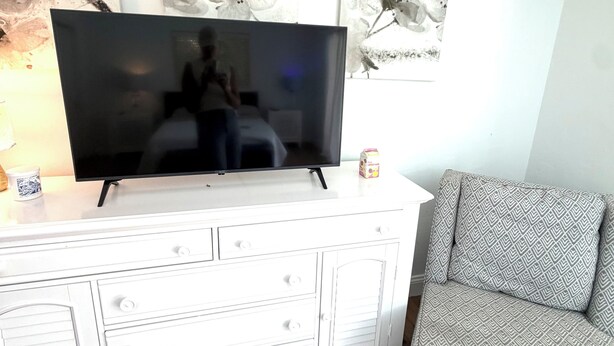 Olohuone, jossa on valkoinen TV-taso ja siinä litteänäyttöinen televisio, kuviollinen sohva ja taideteoksia seinällä.