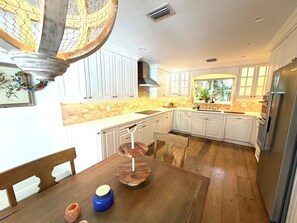 Une cuisine avec des meubles blancs, une table à manger en bois et un four encastré.