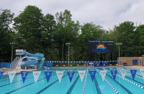 A swimming pool area with lane dividers, a water slide, and a sign for Forest Park Aquatic Center.