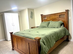 A wooden bed with a green bedspread in a room with a white wardrobe and a wall-mounted decorative leaf.