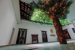 Un edificio con un árbol grande en el centro, un cartel con un logotipo y un piso de baldosas.