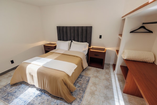 A bedroom with a bed, bedside tables, a hanging closet, and a patterned rug.