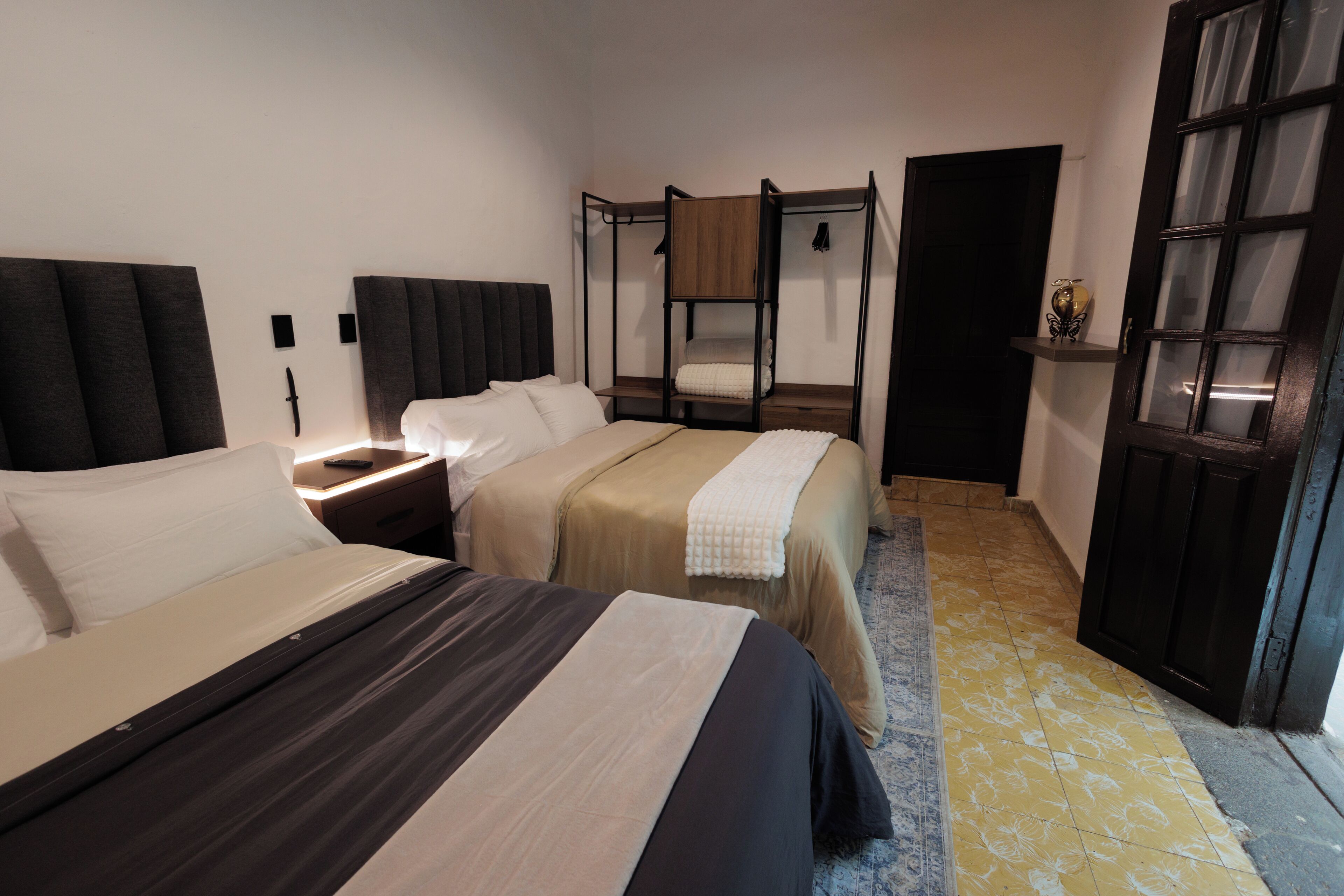 Una habitación de hotel con dos camas, una mesita de noche, un armario y una puerta con paneles de vidrio.