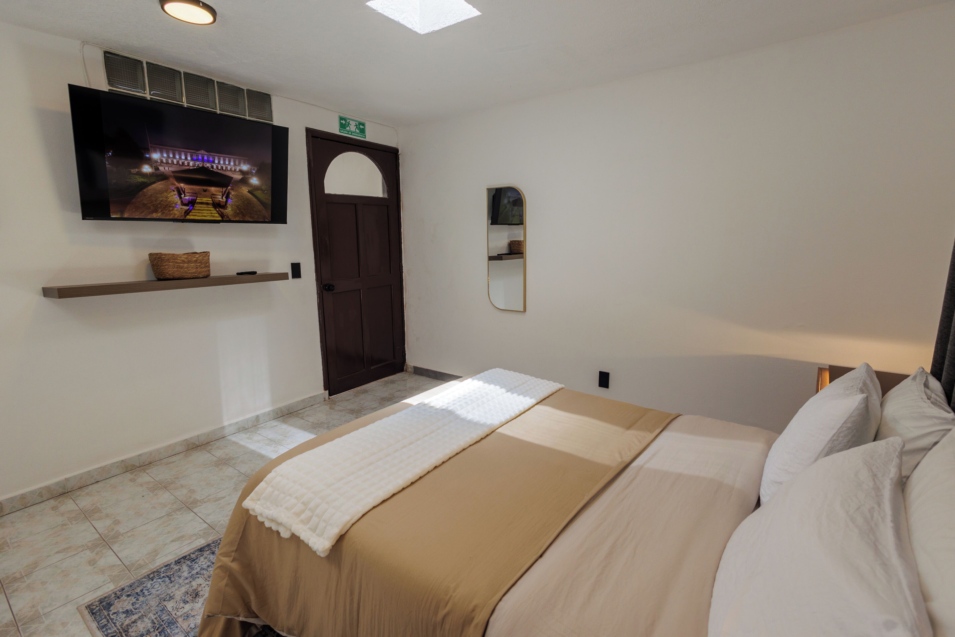 Een hotelkamer met een bed, een aan de muur bevestigde televisie, een deur en een klein plankje.