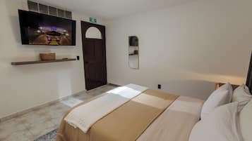 Een hotelkamer met een bed, een aan de muur bevestigde televisie, een deur en een klein plankje.