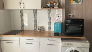 A compact kitchen with a built-in washing machine, a toaster, and a microwave on the countertop. - 2 BED BEACH HUT+ STUDIO+SWIMSPA,SAUNA,PATROLLED BEACH,TAVERN, SHOPS,RESTAURANTS. (Tannum Sands)
