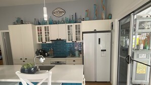 A kitchen with white cabinets, a blue backsplash, and a refrigerator. - 2 BED BEACH HUT+ STUDIO+SWIMSPA,SAUNA,PATROLLED BEACH,TAVERN, SHOPS,RESTAURANTS. (Tannum Sands)