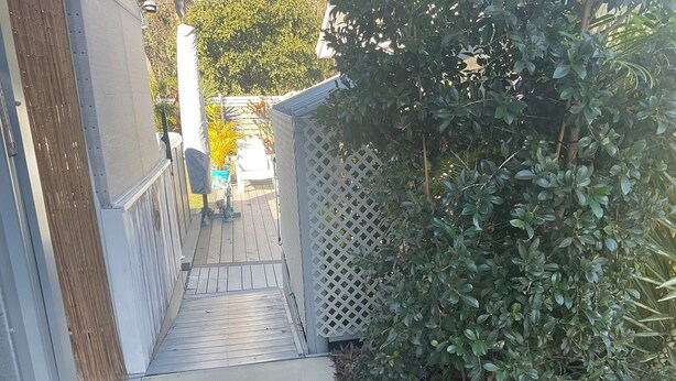 A narrow pathway leading to a wooden deck with a lattice fence on one side and dense foliage on the other. - 2 BED BEACH HUT+ STUDIO+SWIMSPA,SAUNA,PATROLLED BEACH,TAVERN, SHOPS,RESTAURANTS. (Tannum Sands)
