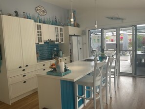 A kitchen with white cabinetry, a blue backsplash, and a dining area with white chairs and a table.