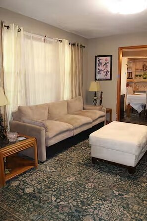 Una sala de estar con sofá, reposapiés, lámpara y alfombra estampada.