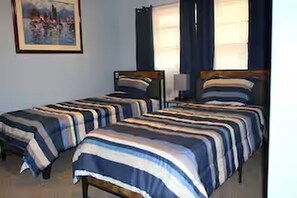 Een kamer met twee bedden, elk voorzien van gestreepte lakens, een schilderij aan de muur en een raam met gordijnen.