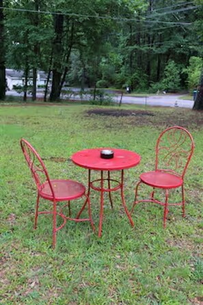 A red metal table and two chairs in a grassy outdoor area with trees in the background. - 3-bedroom house in adorable College Park with AC (College Park)