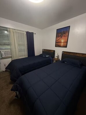 A hotel room with two beds, a window with curtains, an air conditioning unit, and a wall-mounted picture. - 3-bedroom house in adorable College Park with AC (College Park)