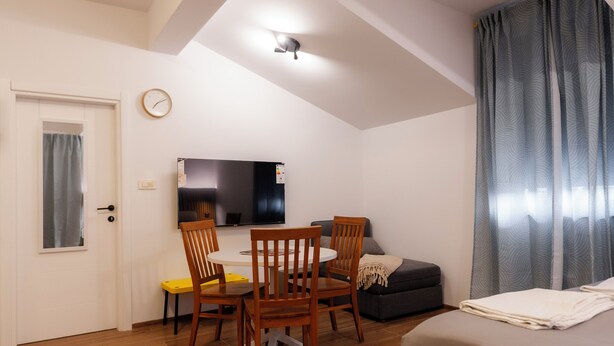Habitación compacta con cama, una mesa de comedor con sillas, televisor y ventana con cortinas.