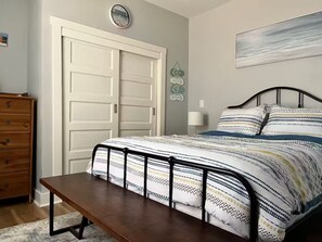 A bedroom with a bed, a bench, a dresser, a wall clock, and a painting. - Dino's Place - Minutes from Downtown Houston. (Houston)