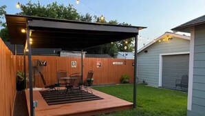 Une terrasse à l’arrière de la maison, avec une plateforme en bois, des chaises en métal et une table.
